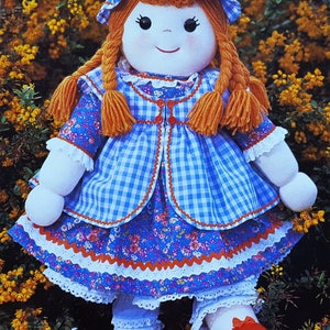 May include: A handmade rag doll with a blue and white gingham dress, red shoes, and orange braids. The doll is wearing a white lace trimmed petticoat and a blue and white gingham bonnet with a red bow.