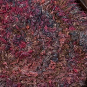 Puede incluir: Primer plano de una alfombra texturizada con una mezcla de colores que incluyen rosa, rojo, marrón y azul. La alfombra tiene un aspecto peludo y está colocada en un cuenco de madera.