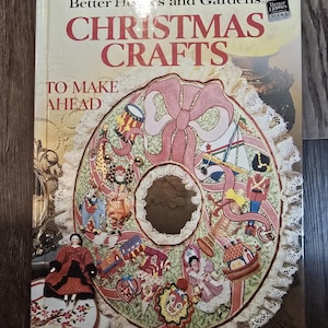 May include: A vintage book titled "Christmas Crafts" by Better Homes and Gardens. The cover features a festive wreath design with a large pink bow and various Christmas-themed illustrations. The book is a guide to making Christmas crafts.