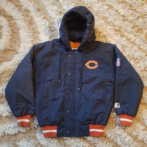 May include: Navy blue Chicago Bears hooded jacket with orange and white accents. Features the team's logo on the chest and a Starter logo. The jacket has a button-up front, a hood, and ribbed cuffs and hem.