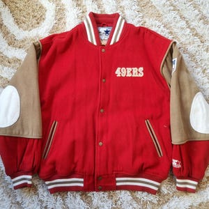 May include: Red and tan varsity jacket with the text "49ERS" in white. The jacket has tan sleeves with white elbow patches and a white and brown striped collar, cuffs, and hem. A Star logo is visible on the collar.