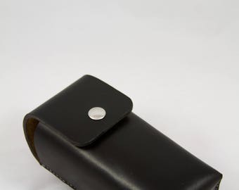 May include: A black leather eyeglasses case with a silver snap closure. The rectangular case has rounded edges and a flap that secures with a single, circular silver snap. The case is designed to protect eyewear.
