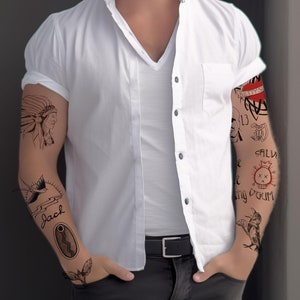 May include: A man with a white button-down shirt and black pants has several tattoos on his arms. The tattoos include a Native American chief, a bird, a skull, and a heart.
