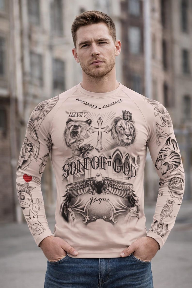 May include: A long-sleeved, beige shirt featuring a detailed tattoo-style design. The artwork includes a bear, lion, cross, eagle, and the text "SON OF GOD" and "Purpose". Additional tattoos are visible on the sleeves.