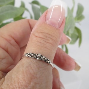 May include: A silver ring with an ornate design is worn on a finger. The ring features a series of decorative elements, including small beads and intricate patterns. The ring is a delicate piece of jewelry.