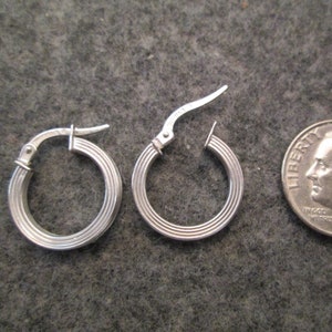 May include: A pair of silver hoop earrings with a ridged design. The earrings are about the size of a dime.