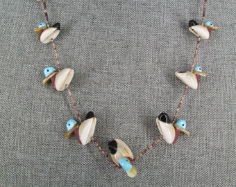 May include: A necklace made of shell and turquoise beads, featuring a design of small birds. The necklace is brown and white with blue accents.