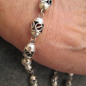 May include: Silver bracelet with oval-shaped links, each with an intricate design. The links are connected by small silver chains.