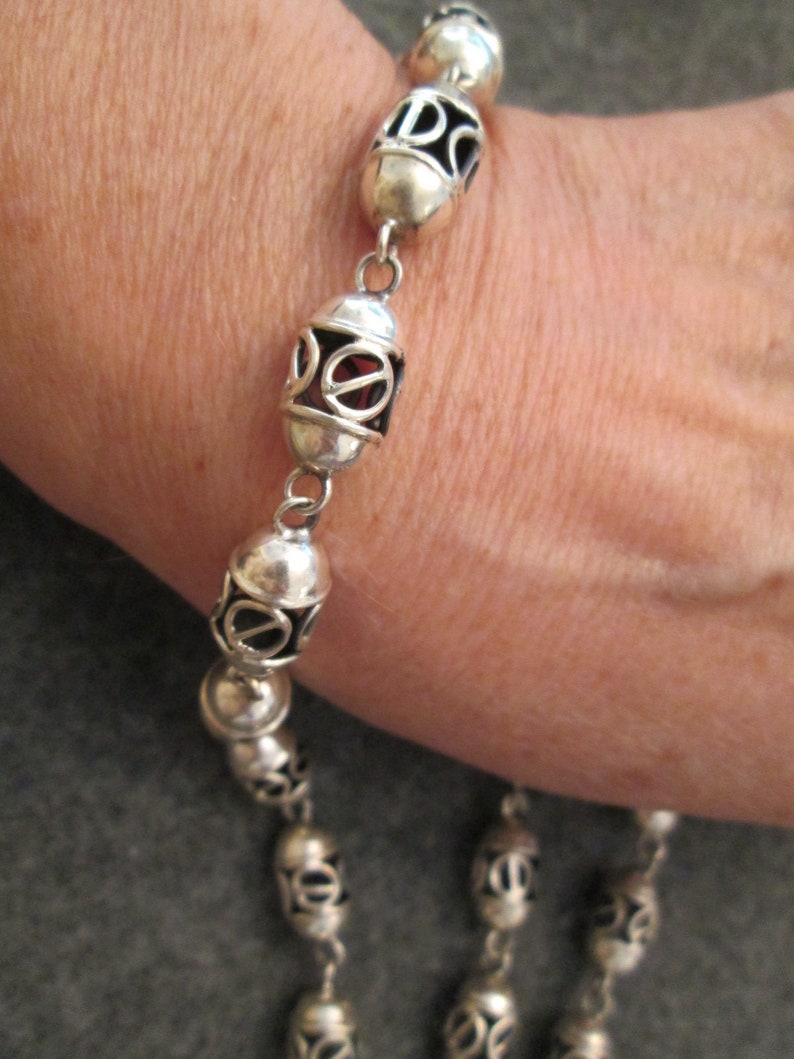 May include: Silver bracelet with oval-shaped links, each with an intricate design. The links are connected by small silver chains.