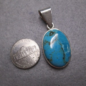 Puede incluir: Un colgante de plata con una piedra turquesa azul. La piedra es de forma ovalada y tiene un color azul claro con vetas azules m&aacute;s oscuras. El colgante es aproximadamente del tama&ntilde;o de una moneda de un c&eacute;ntimo de euro.