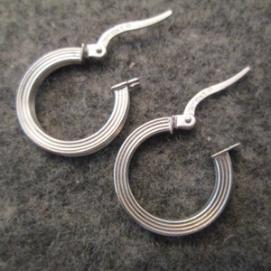 May include: A pair of silver hoop earrings with a ridged design. The earrings have a hinged closure.