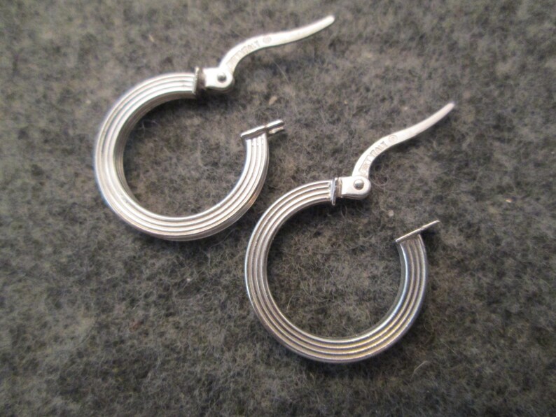 May include: A pair of silver hoop earrings with a ridged design. The earrings have a hinged closure.