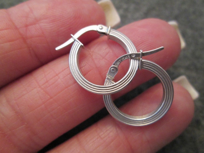 May include: Silver hoop earrings with a ridged design and a hinged clasp. The earrings are marked "Italy".