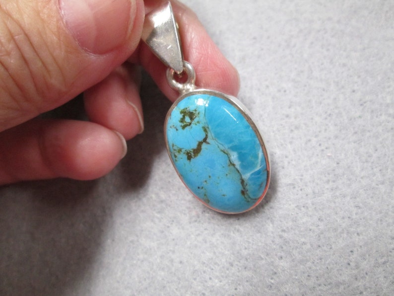 Puede incluir: Un colgante de plata con una piedra turquesa azul. La piedra tiene un patr&oacute;n de m&aacute;rmol con vetas blancas y marrones.