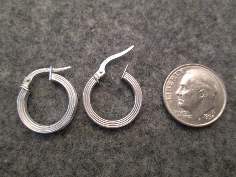 May include: A pair of silver hoop earrings with a ridged design. The earrings are about the size of a dime.