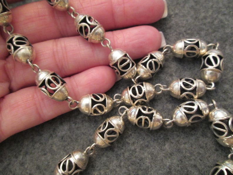 May include: A silver chain necklace with oval-shaped links. Each link has a delicate, openwork design.
