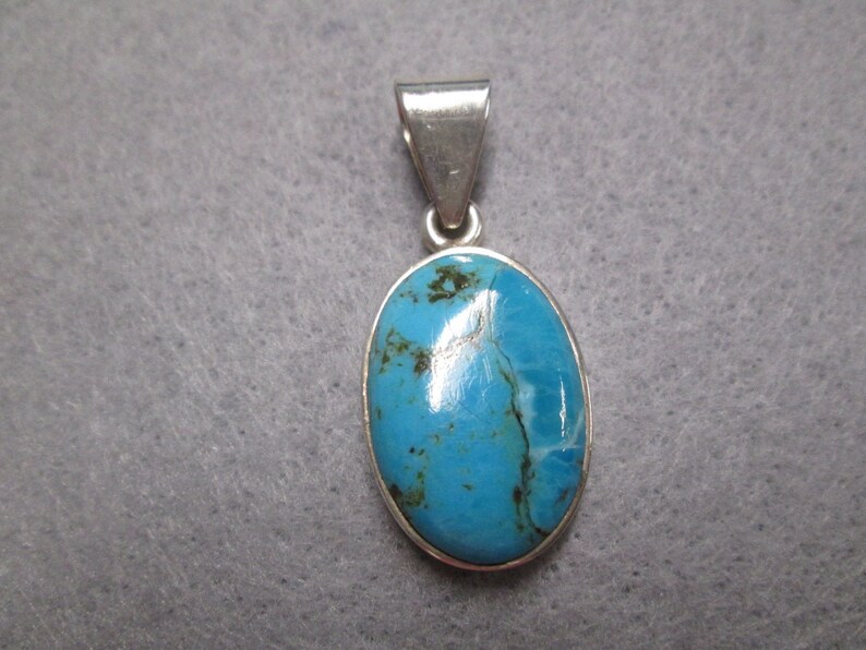 Puede incluir: Un colgante de plata con una piedra ovalada turquesa azul.