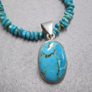 Puede incluir: Un collar con un colgante de turquesa con engaste de plata. El colgante tiene forma ovalada y presenta una piedra turquesa azul con vetas marrones y blancas. El collar est&aacute; hecho de cuentas de turquesa.