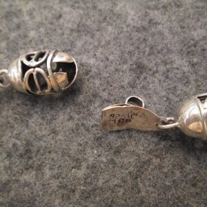 May include: A silver necklace with a decorative clasp and a pendant with a circular design. The clasp is marked "925 Italy".