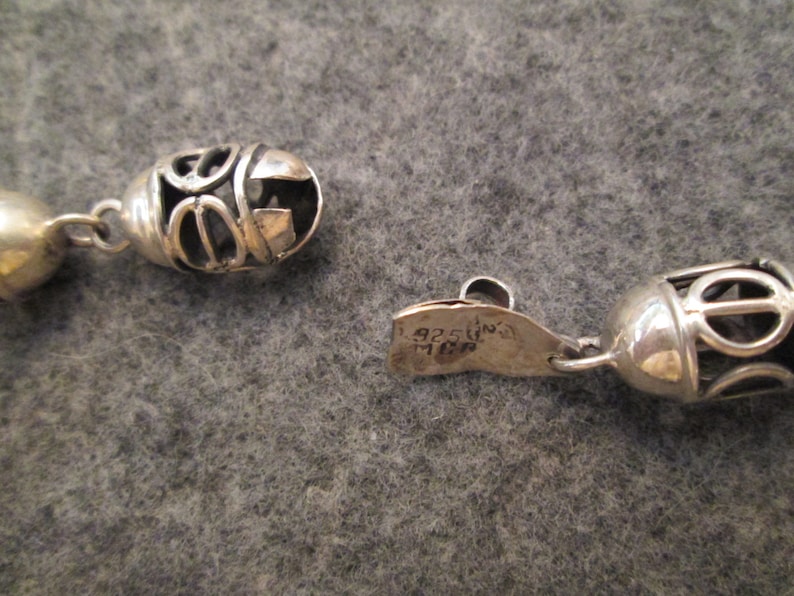 May include: A silver necklace with a decorative clasp and a pendant with a circular design. The clasp is marked "925 Italy".