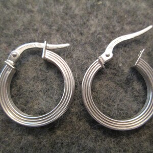 May include: A pair of silver hoop earrings with a ridged design. The earrings have a hinged closure.