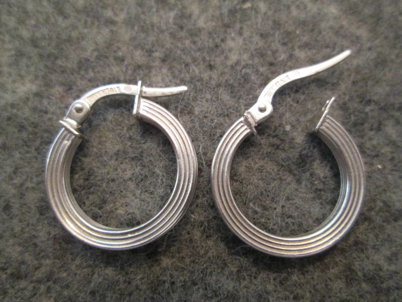May include: A pair of silver hoop earrings with a ridged design. The earrings have a hinged closure.