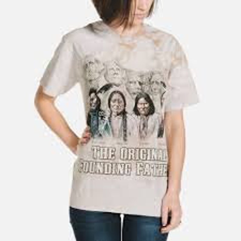 Op de afbeelding: Een wit tie-dye T-shirt met een grafische print van zes gezichten van Amerikaanse indianen. De tekst "The Original Founding Fathers" is onder de print gedrukt.