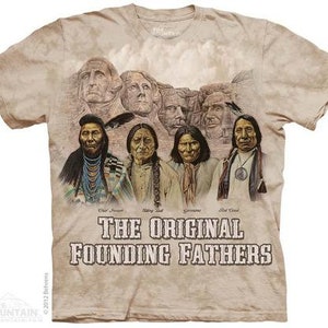 Op de afbeelding: Een beige T-shirt met een vervaagde print van het Mount Rushmore National Memorial. De afbeelding toont de gezichten van vier presidenten: George Washington, Thomas Jefferson, Theodore Roosevelt en Abraham Lincoln. Onder de afbeelding staat de tekst "The Original Founding Fathers".