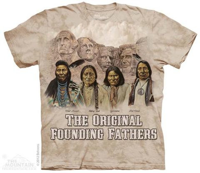 Op de afbeelding: Een beige T-shirt met een vervaagde print van het Mount Rushmore National Memorial. De afbeelding toont de gezichten van vier presidenten: George Washington, Thomas Jefferson, Theodore Roosevelt en Abraham Lincoln. Onder de afbeelding staat de tekst "The Original Founding Fathers".