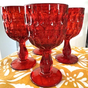May include: Three matching red glass goblets featuring a prominent embossed honeycomb or dot pattern on the bowl. Each goblet has a thick, faceted stem and a circular base, crafted from translucent red glass with a consistent deep crimson hue.
