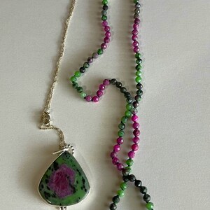 May include: A green and pink gemstone necklace with a matching pendant. The pendant is a teardrop shape and the necklace is made of faceted beads.