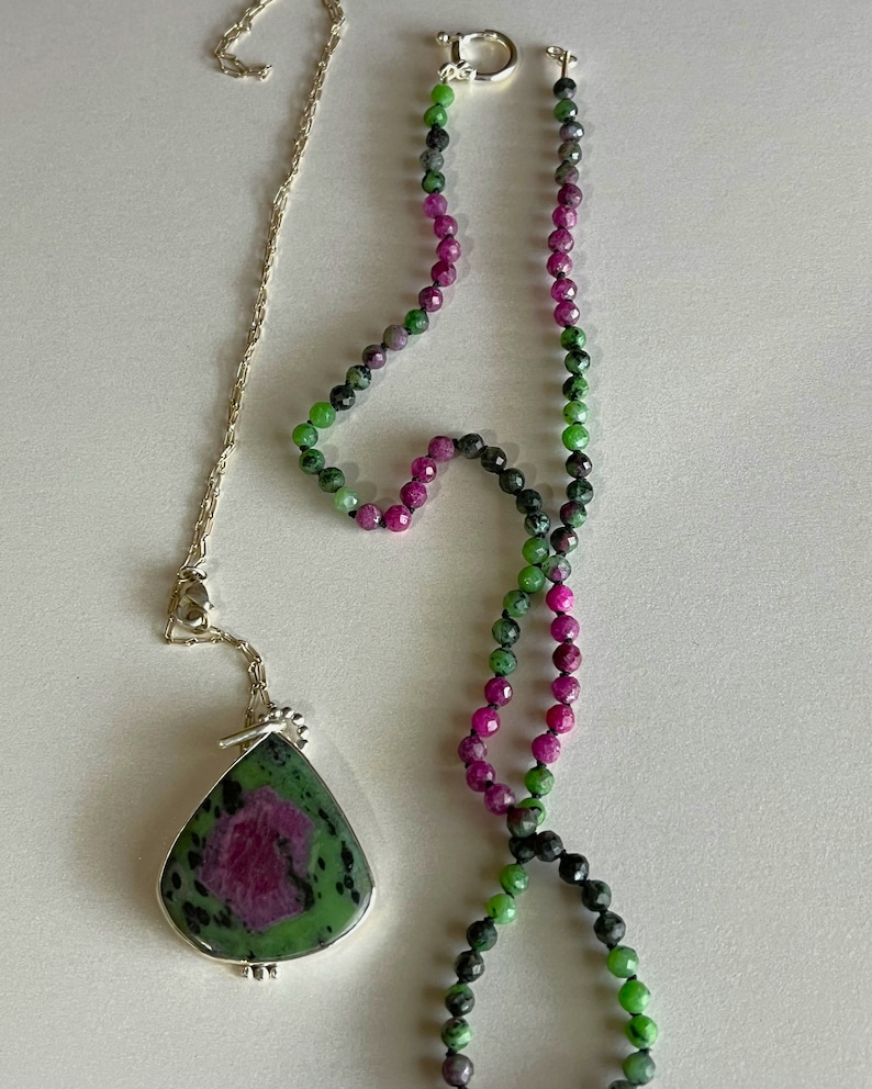 May include: A green and pink gemstone necklace with a matching pendant. The pendant is a teardrop shape and the necklace is made of faceted beads.
