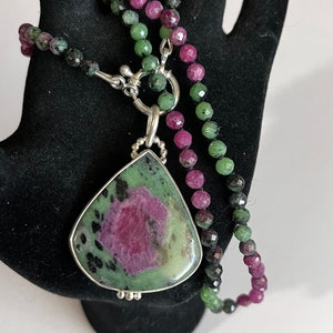 May include: A green and pink gemstone pendant necklace with a silver clasp. The necklace is made of green, pink, and black beads.