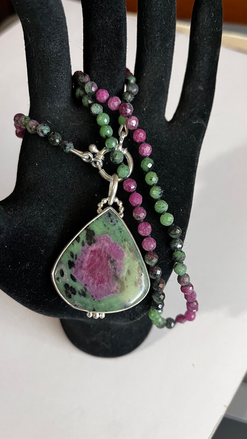 May include: A green and pink gemstone pendant necklace with a silver clasp. The necklace is made of green, pink, and black beads.