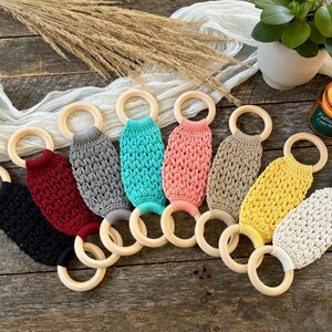 Puede incluir: Ocho mordedores de crochet con anillos de madera. Los mordedores son de varios colores, incluyendo negro, rojo, gris, azul verdoso, rosa, beige, amarillo y blanco.