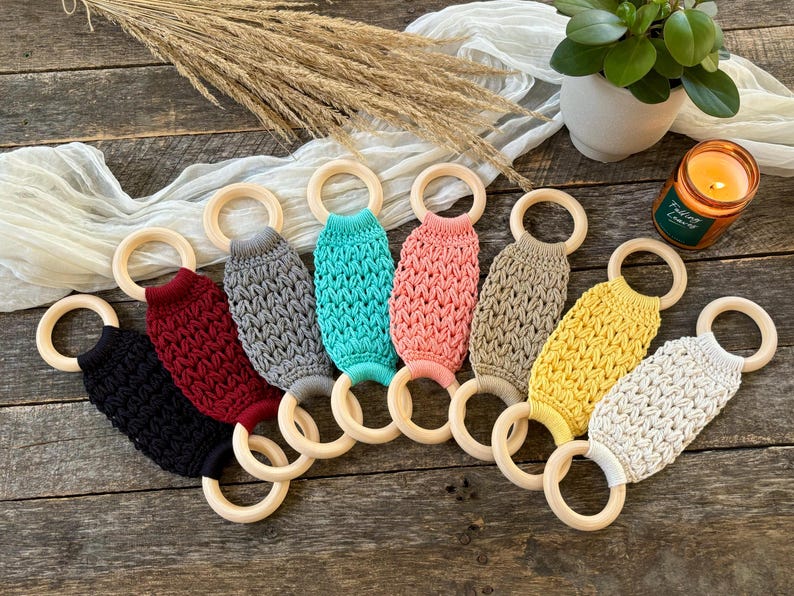 Puede incluir: Ocho mordedores de crochet con anillos de madera. Los mordedores son de varios colores, incluyendo negro, rojo, gris, azul verdoso, rosa, beige, amarillo y blanco.
