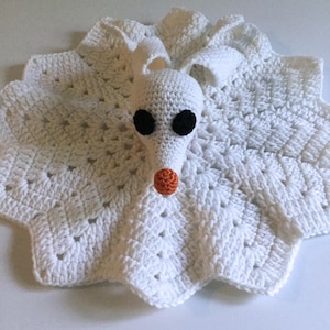May include: White crocheted baby blanket with a white crocheted ghost character attached. The ghost has black eyes and an orange nose.
