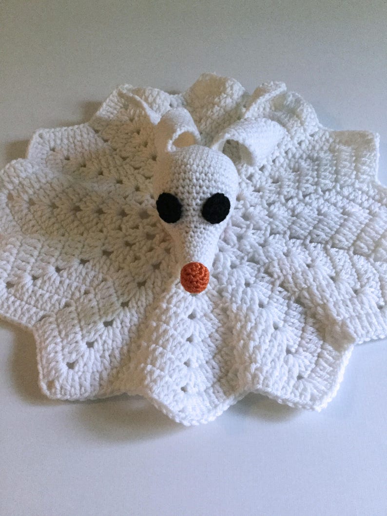 May include: White crocheted baby blanket with a white crocheted ghost character attached. The ghost has black eyes and an orange nose.