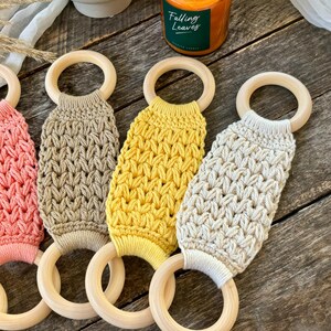 Puede incluir: Cuatro mordedores de crochet en diferentes colores, incluyendo rosa, beige, amarillo y crema, unidos a anillos de madera. Los mordedores est&aacute;n hechos con un patr&oacute;n de puntada texturizado.