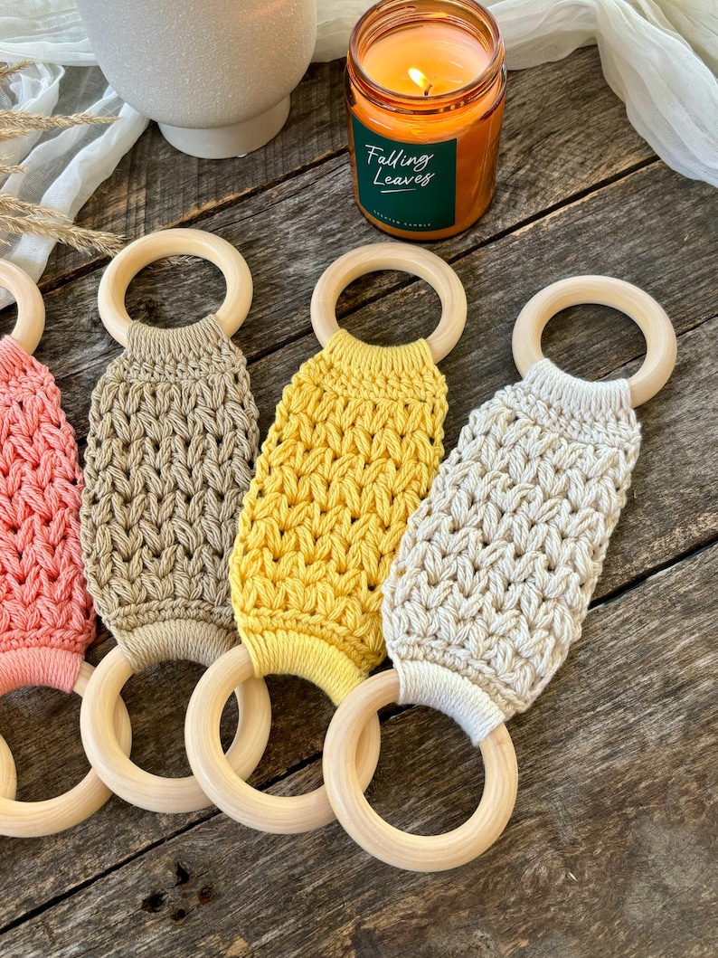 Puede incluir: Cuatro mordedores de crochet en diferentes colores, incluyendo rosa, beige, amarillo y crema, unidos a anillos de madera. Los mordedores est&aacute;n hechos con un patr&oacute;n de puntada texturizado.