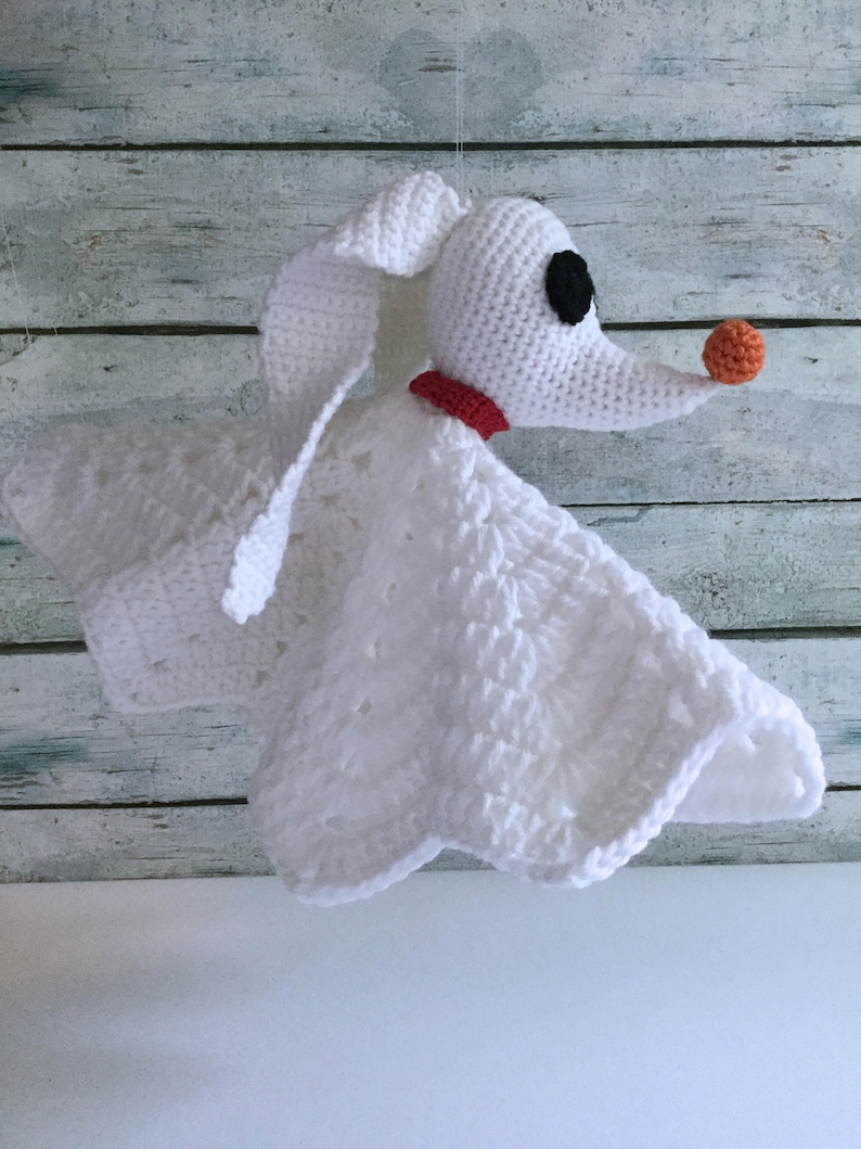 May include: White crocheted blanket with a plush, white crocheted dog head attached. The dog has black eyes, a red collar, and an orange nose.