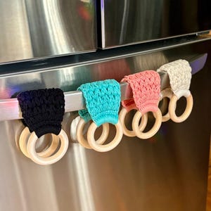 Puede incluir: Cinco cubiertas de manijas de refrigerador de ganchillo en negro, turquesa, rosa, beige y blanco con anillos de madera.