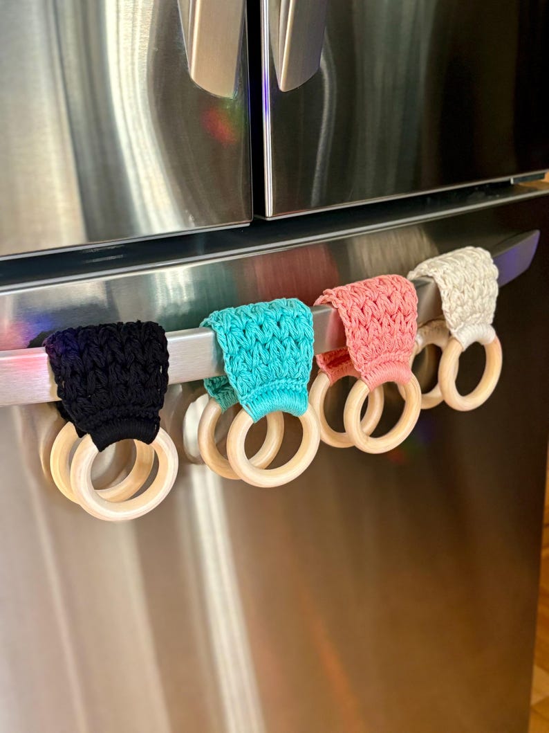 Puede incluir: Cinco cubiertas de manijas de refrigerador de ganchillo en negro, turquesa, rosa, beige y blanco con anillos de madera.