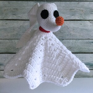 May include: White crocheted baby blanket with a crocheted Zero the Ghost Dog from The Nightmare Before Christmas attached. Zero has black eyes and an orange nose.