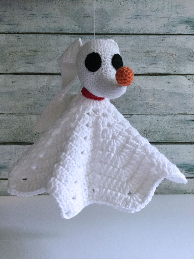 May include: White crocheted baby blanket with a crocheted Zero the Ghost Dog from The Nightmare Before Christmas attached. Zero has black eyes and an orange nose.