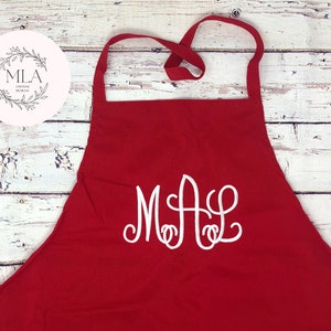 Puede incluir: Delantal de cocina rojo con un monograma bordado en blanco "MAL" en la parte delantera.
