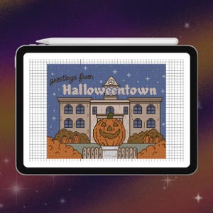 Puede incluir: Una tableta digital que muestra un patrón de punto de cruz de un edificio con el texto "greetings from Halloweentown" encima. Una gran calabaza de Halloween está en primer plano, rodeada de calabazas más pequeñas y una valla blanca.