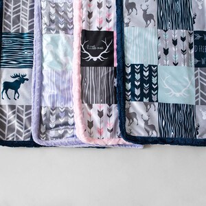 May include: A collection of patchwork baby blankets with various patterns and colors. Designs include arrows, deer, and wood grain. The blankets have a soft, plush texture and are trimmed with a dark blue border. One blanket has the text "little one".