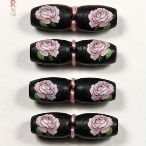May include: Four black wooden beads with a pink rose design. Each bead has a pink rose with green leaves painted on it. The beads are connected in pairs with pink string.