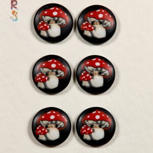 May include: Six round black buttons with a painted mushroom design. Each button features a red mushroom cap with white spots, a smaller red mushroom, and a white mushroom stem. The buttons are arranged on a white card.